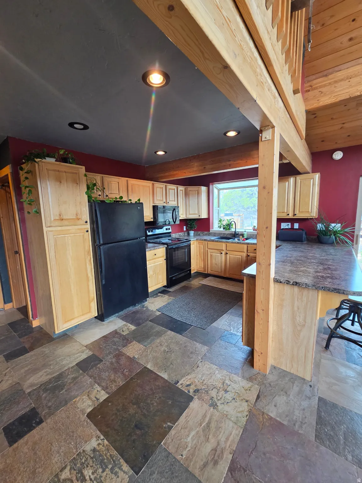 Kitchen featuring natural wood-finish cabinetry, black appliances, and a multi-toned stone tile floor