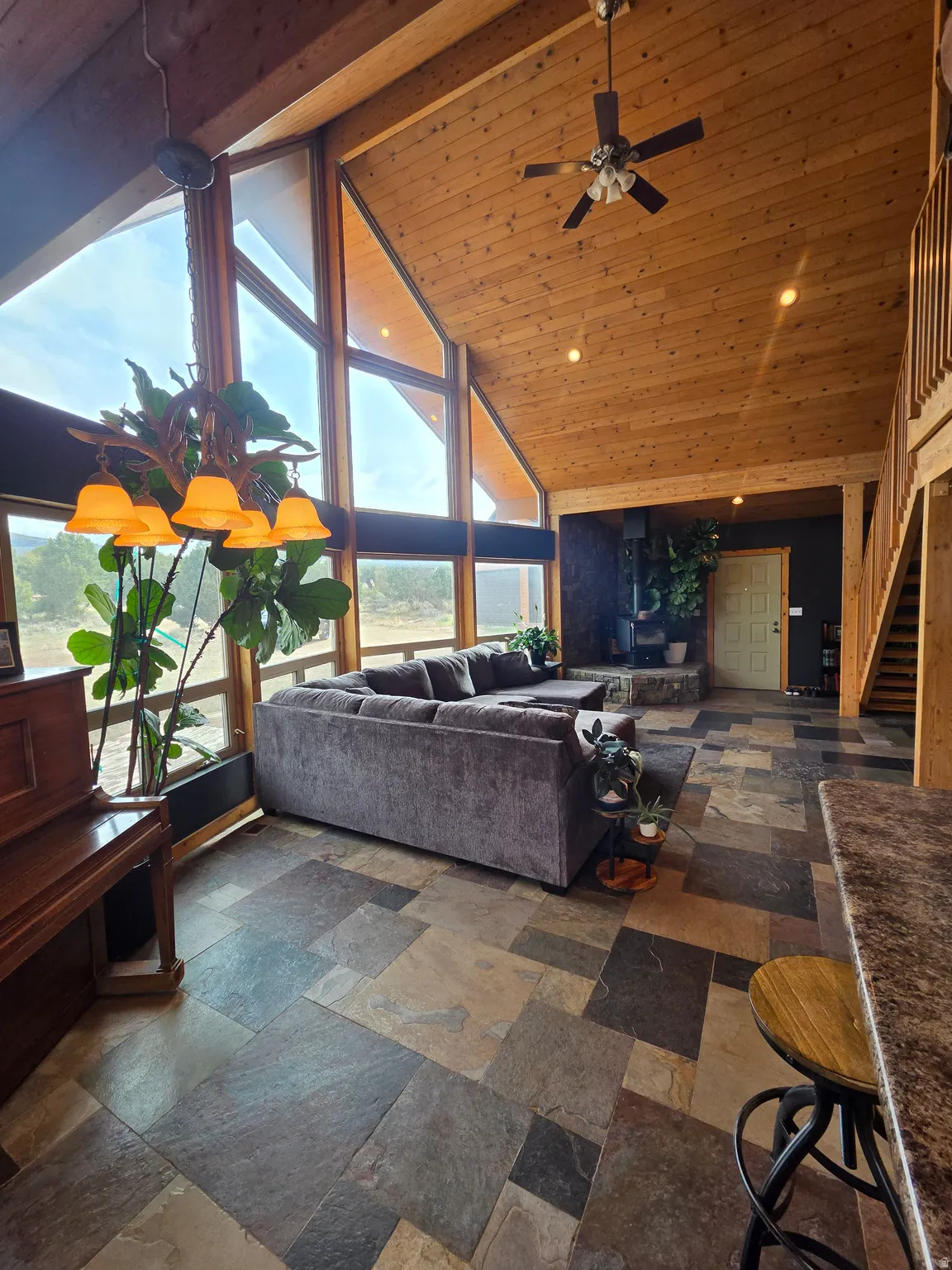 Vaulted tongue & groove ceilings featuring a ceiling fan, expansive wall of windows, multi-tone slate tile flooring, and a wooden staircase with railing
