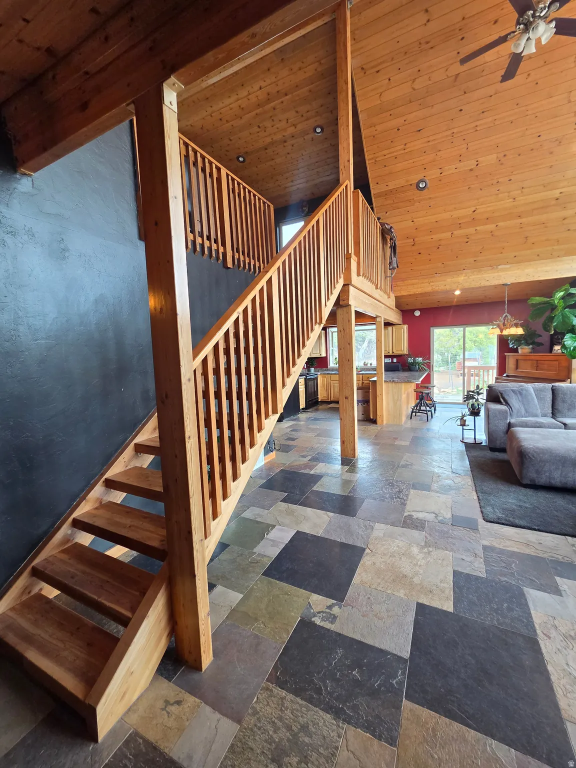 Vaulted tongue & groove ceilings featuring a ceiling fan, expansive wall of windows, multi-tone slate tile flooring, and a wooden staircase with railing