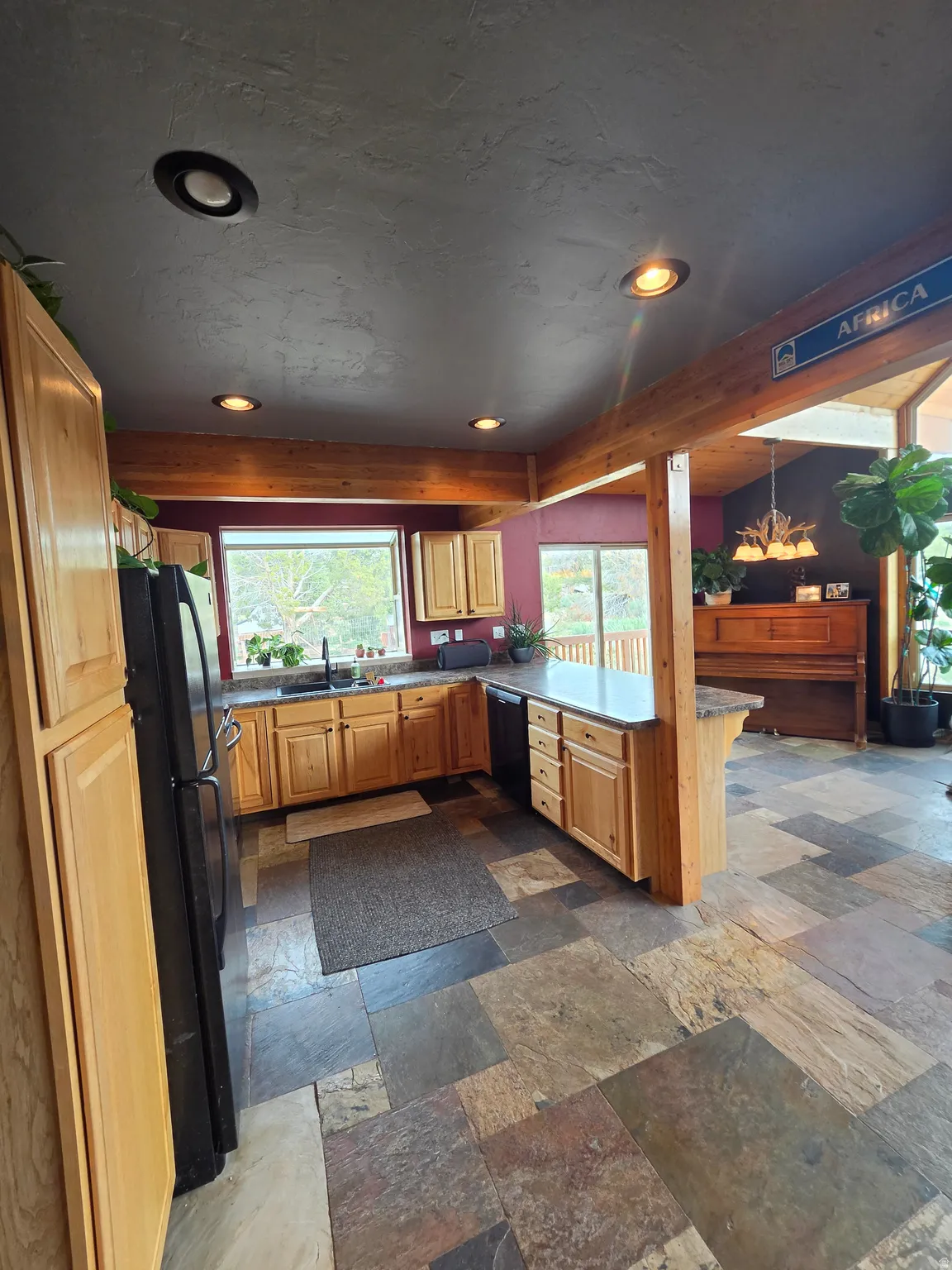 Kitchen featuring natural wood-finish cabinetry, black appliances, and a multi-toned stone tile floor