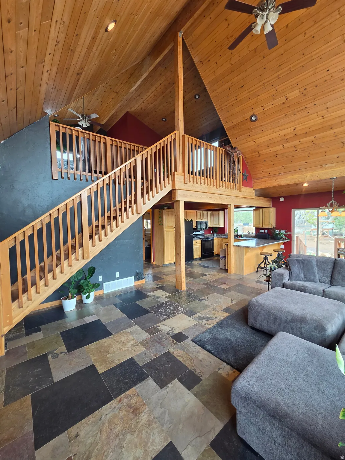 Vaulted tongue & groove ceilings featuring a ceiling fan, expansive wall of windows, multi-tone slate tile flooring, and a wooden staircase with railing