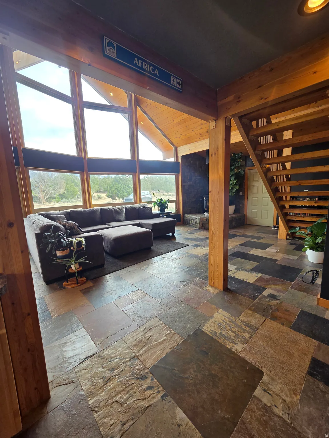 Vaulted tongue & groove ceilings featuring a ceiling fan, expansive wall of windows, multi-tone slate tile flooring, and a wooden staircase with railing
