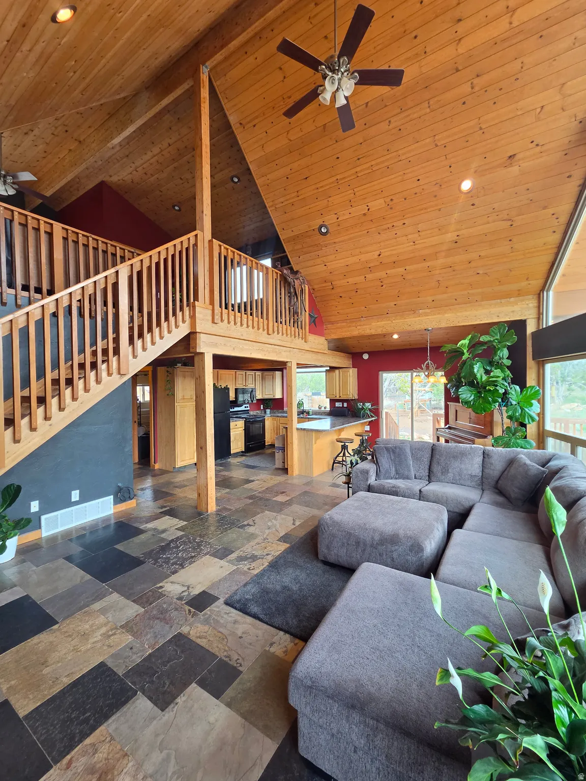 Vaulted tongue & groove ceilings featuring a ceiling fan, expansive wall of windows, multi-tone slate tile flooring, and a wooden staircase with railing