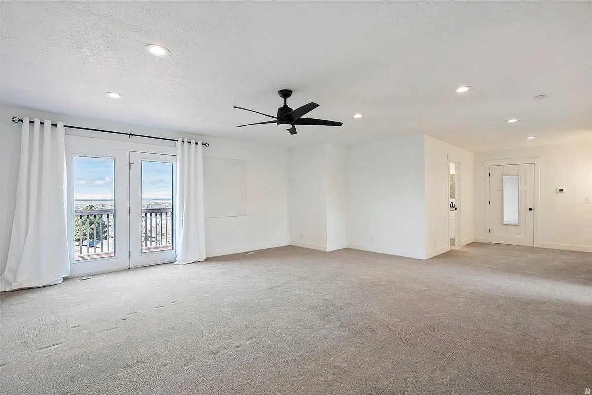 Spacious room featuring light gray carpet flooring, white walls, recessed lighting, and a black ceiling fan