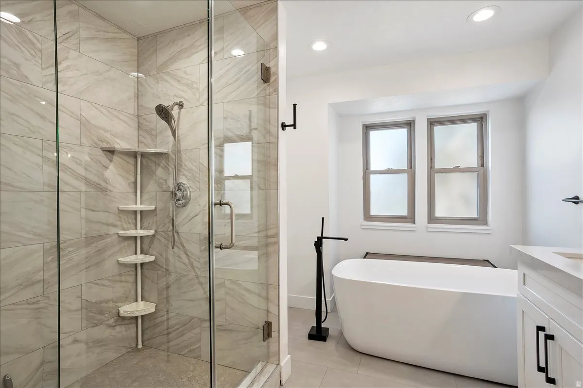 Contemporary bathroom featuring a freestanding tub with a matte black floor-mounted filler, a glass-enclosed shower with tiled walls, and a light-toned vanity with a white countertop