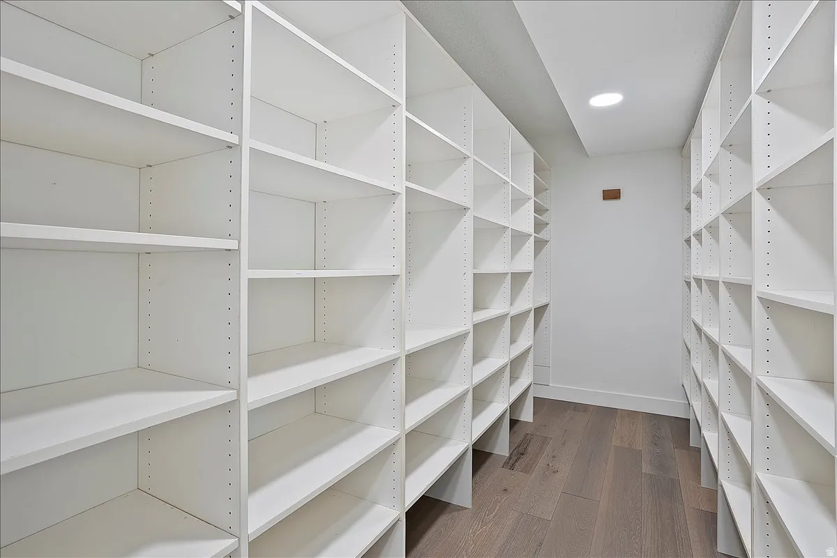 Expansive custom closet featuring extensive adjustable shelving, recessed ceiling lighting, and wood-finish flooring