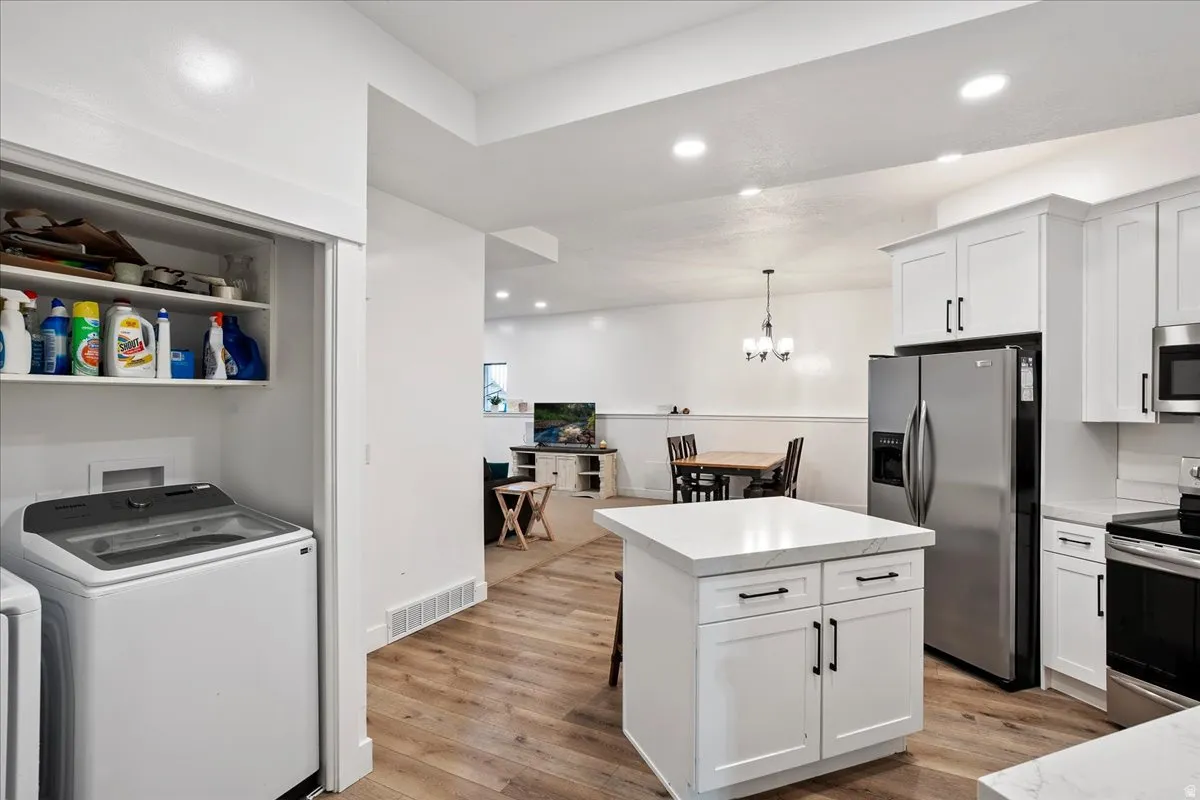 Open-concept kitchen and laundry area featuring wood-finish flooring, white cabinetry, stainless steel appliances, a center island with countertop, and recessed lighting