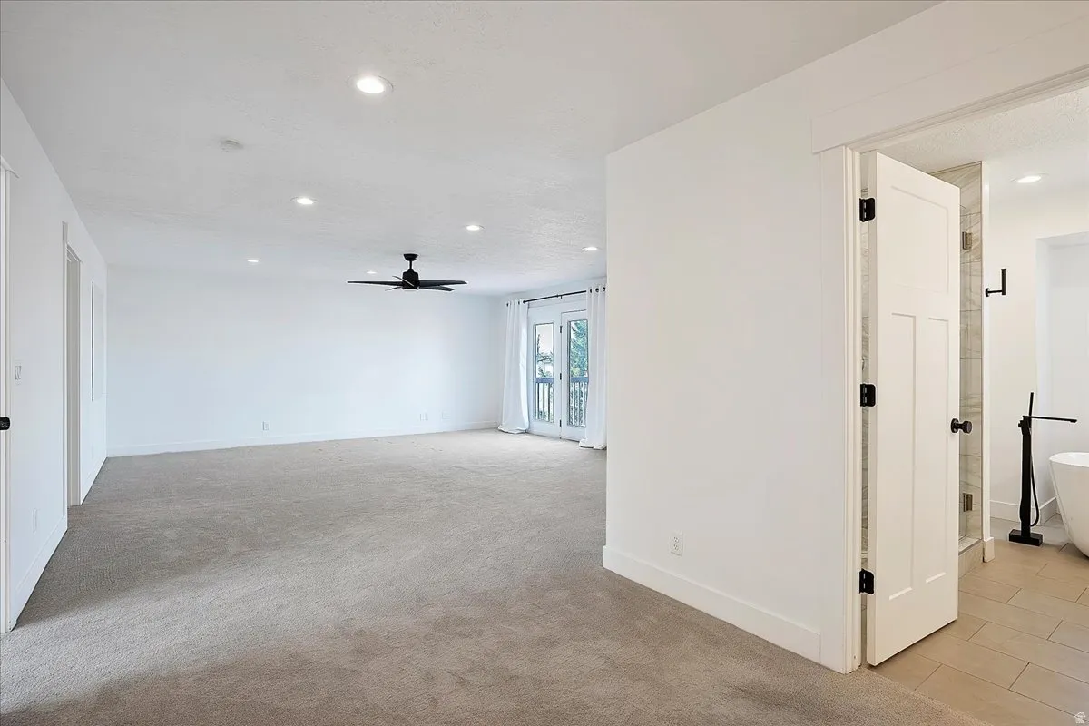 Spacious carpeted room featuring recessed lighting, a ceiling fan, and French doors leading to an exterior balcony