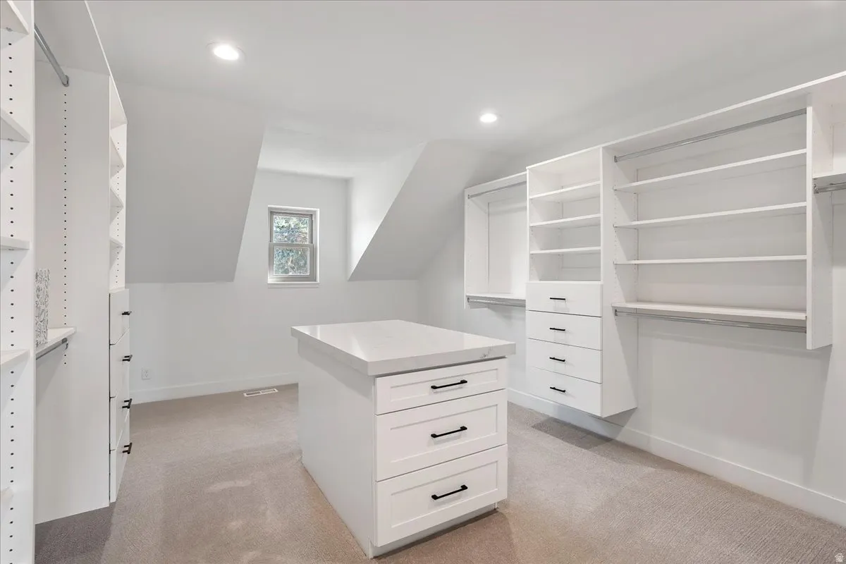 Spacious  walk-in closet featuring a central island with drawers, white built-in shelving, hanging rods, and recessed lighting