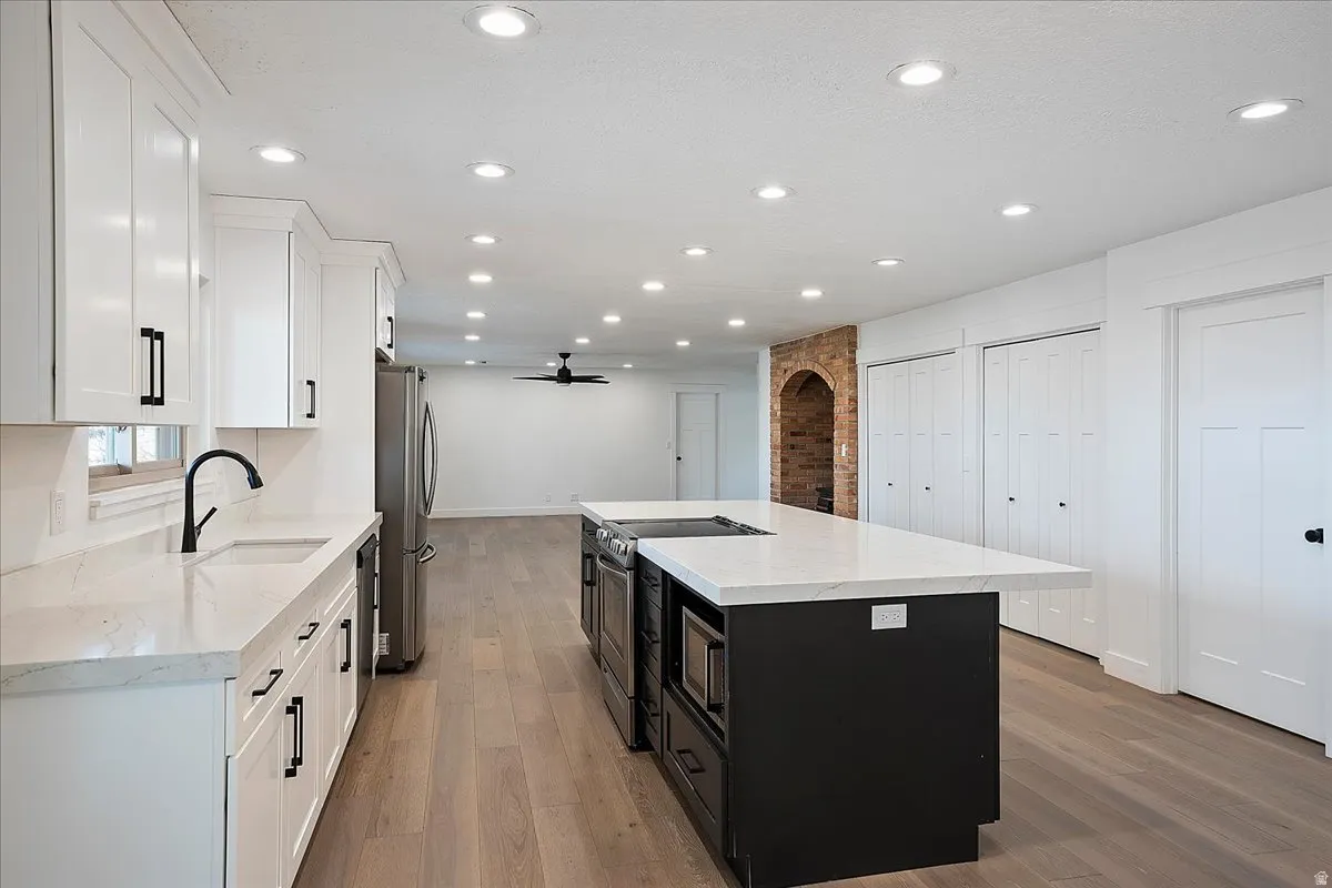 Spacious kitchen featuring an expansive island, white cabinetry with matte black hardware, stainless steel appliances, and recessed lighting
