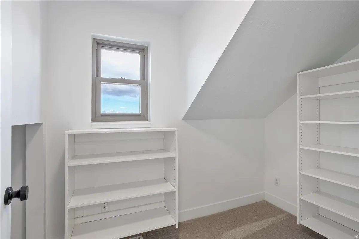 Compact room featuring a single window, two built-in shelving units, a carpeted floor, and an angled ceiling