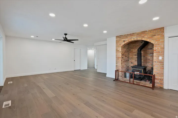 Spacious room featuring wood-finish flooring and a prominent brick fireplace with a wood-burning stove