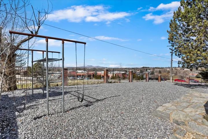 Expansive gravel yard featuring a swing set, mature trees, and a stone patio section