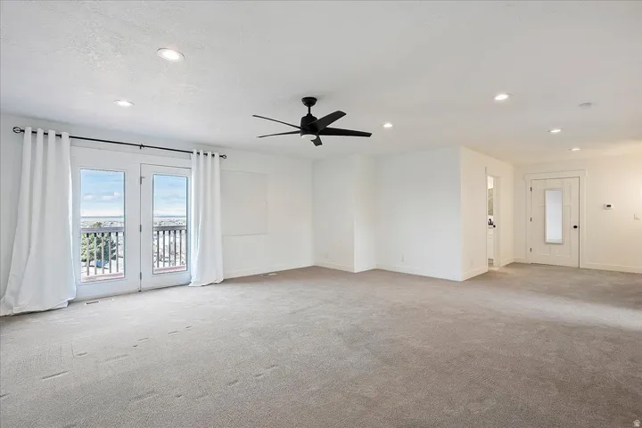 Spacious room featuring light gray carpet flooring, white walls, recessed lighting, and a black ceiling fan