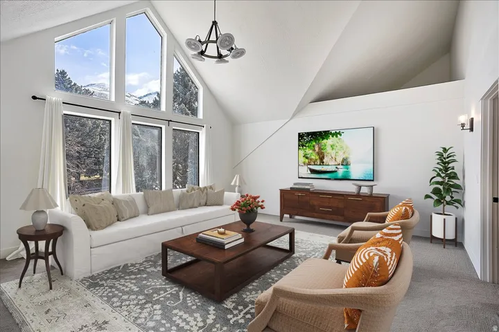Living area featuring vaulted ceilings with exposed beams, oversized windows, a contemporary chandelier, recessed lighting, and soft gray carpeting