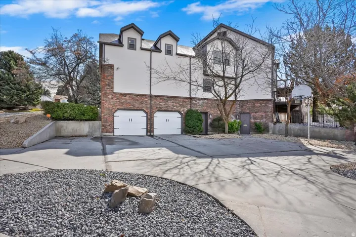 Multi-level property exterior featuring a two-car garage with white paneled doors, brick and stucco facade, and two prominent dormer windows