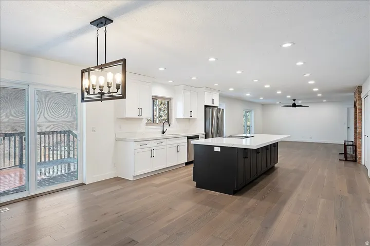 Expansive kitchen featuring a large central island, stainless steel appliances, white cabinetry, and wood-finish flooring