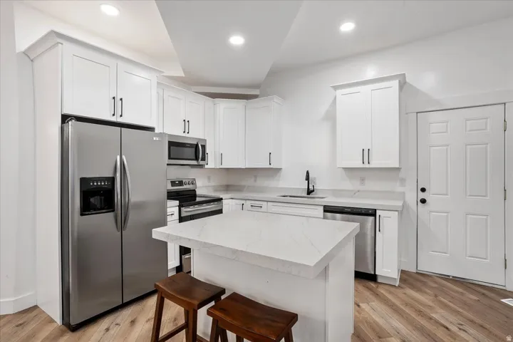 Modern kitchen featuring white shaker cabinetry, stainless steel appliances, light-toned countertops, a central island, and wood-finish flooring