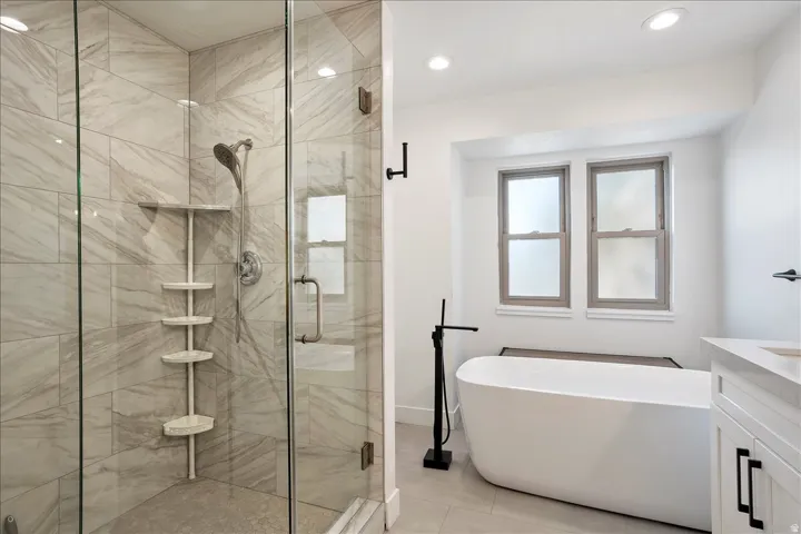 Contemporary bathroom featuring a freestanding tub with a matte black floor-mounted filler, a glass-enclosed shower with tiled walls, and a light-toned vanity with a white countertop