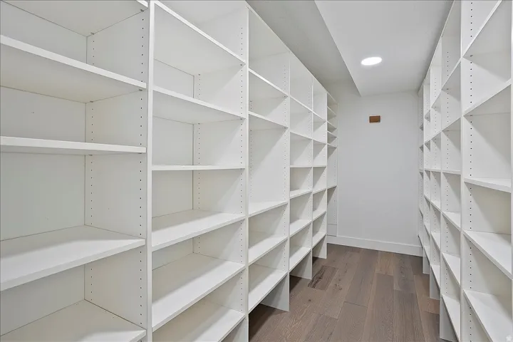 Expansive custom closet featuring extensive adjustable shelving, recessed ceiling lighting, and wood-finish flooring