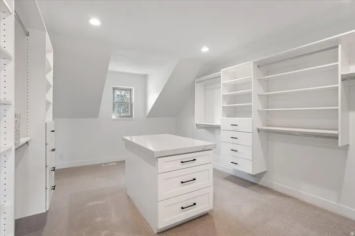 Spacious  walk-in closet featuring a central island with drawers, white built-in shelving, hanging rods, and recessed lighting