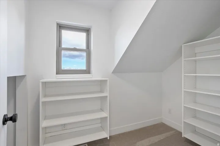 Compact room featuring a single window, two built-in shelving units, a carpeted floor, and an angled ceiling