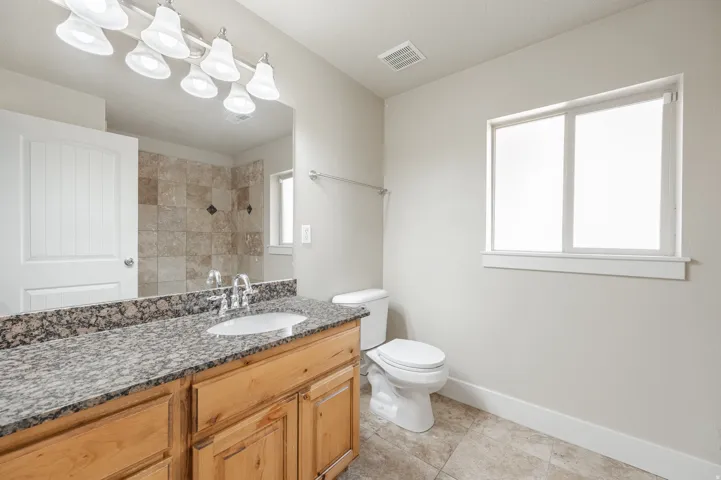 Bathroom featuring a light wood-finish vanity with a granite-style countertop, undermount sink, and polished chrome faucet