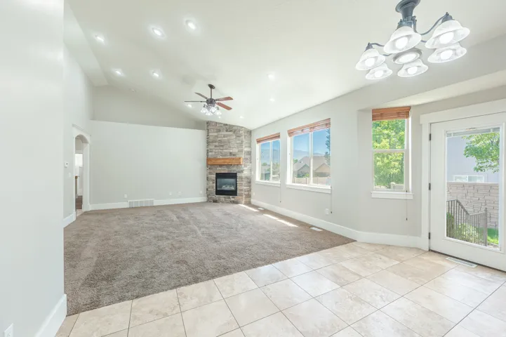 Vaulted ceiling living space featuring a stacked stone fireplace with a wood mantle, recessed lighting, and a ceiling fan