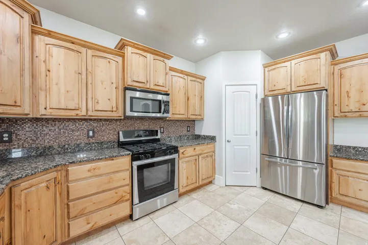 Kitchen featuring light wood cabinetry, stone countertops, a mosaic tile backsplash, stainless steel appliances, and large format tile flooring