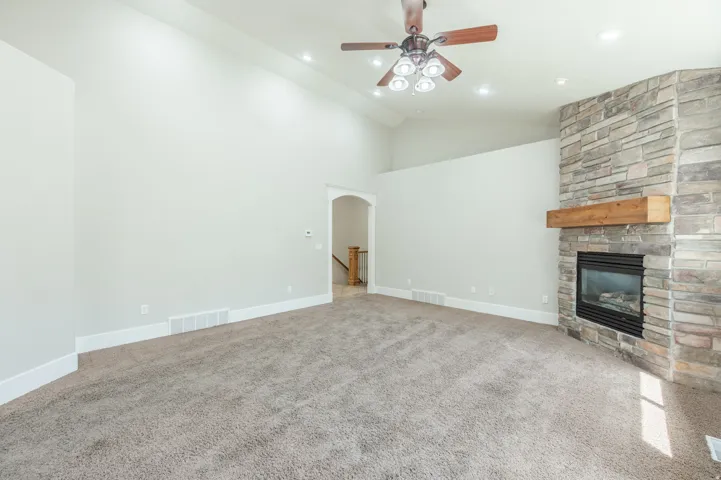 Spacious room featuring a stone-clad fireplace with a wood mantel, high vaulted ceilings, recessed lighting, a ceiling fan, and carpet flooring