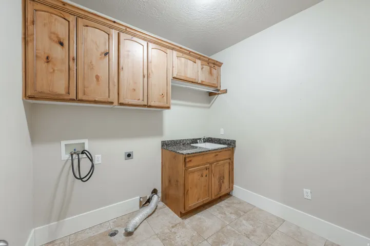 Laundry area featuring wood cabinetry, a utility sink with a granite-look countertop, tile flooring, and a hanging rod