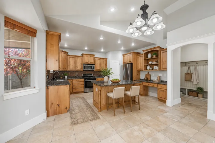 Gourmet kitchen with natural wood cabinetry, dark granite countertops, stainless steel appliances, a central island with seating, and tile flooring