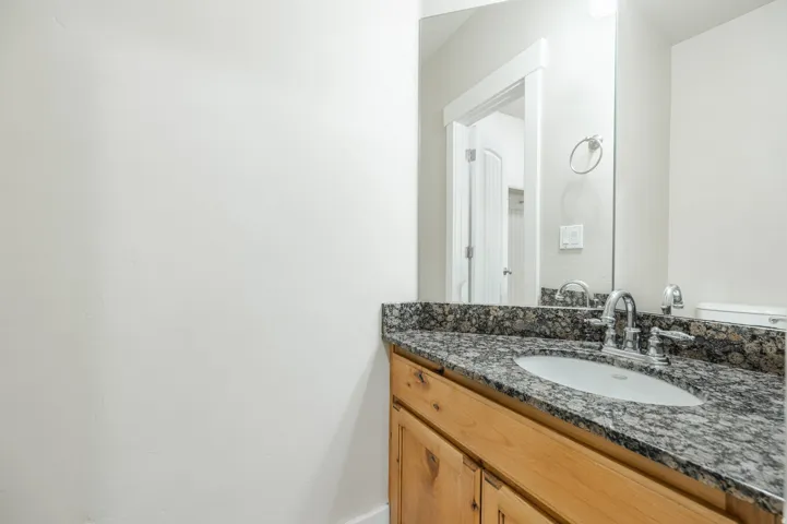 Vanity featuring a polished granite countertop, undermount sink, chrome faucet, and natural wood cabinetry