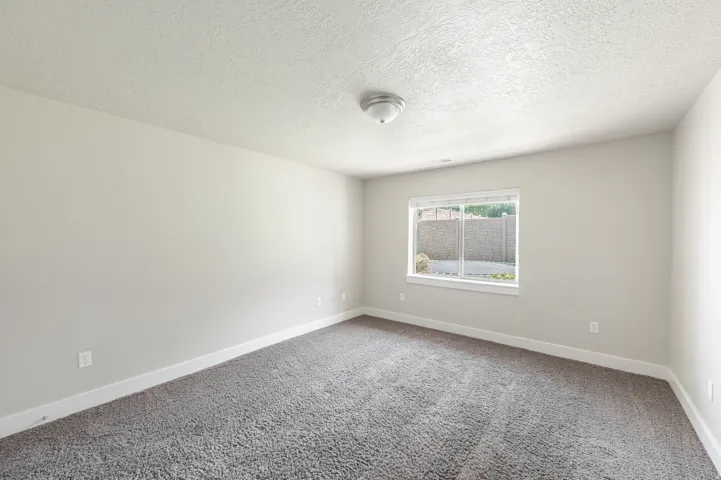 Spacious interior room with neutral-toned walls, textured ceiling, and gray carpet flooring