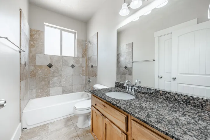 Bathroom featuring a white tub, natural stone tile shower surround with accent tiles, and a window above the tub