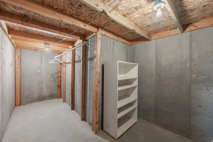 Unfinished basement space featuring exposed wood framing and concrete walls