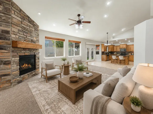 Spacious interior featuring a stone-clad fireplace with a wood mantel, vaulted ceilings with recessed lighting, an open-concept kitchen with wood cabinetry and an island with bar seating, and multiple windows for natural light