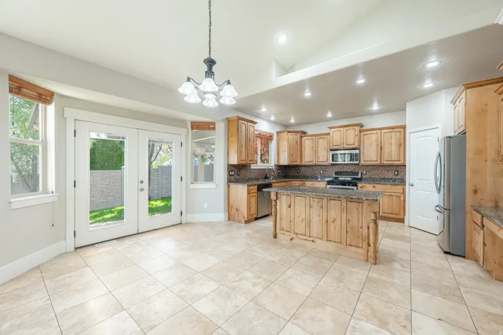Spacious kitchen and dining area featuring tile flooring, light wood cabinetry, a central island with a stone countertop, stainless steel appliances, and French doors opening to the exterior
