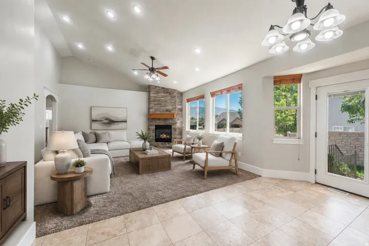 Spacious living area featuring a vaulted ceiling with recessed lighting, a stone-clad fireplace with a wood mantel, and large windows with wood trim