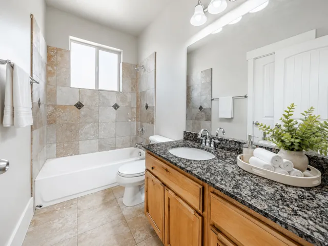 Bathroom featuring a bathtub with tile surround, wood-finish vanity with a dark granite countertop, undermount sink, and large wall-mounted mirror