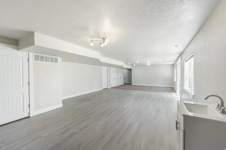Spacious lower-level area featuring light wood-finish flooring, recessed lighting, and a utility sink with a chrome faucet