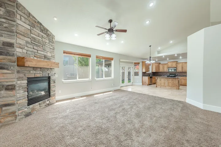 Spacious living area featuring a stone-clad fireplace with a wood mantel, vaulted ceilings, recessed lighting, and a ceiling fan