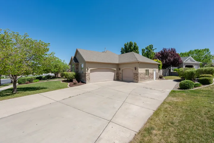 Exterior featuring a multi-car driveway, stone accents, two garage doors, and mature landscaping