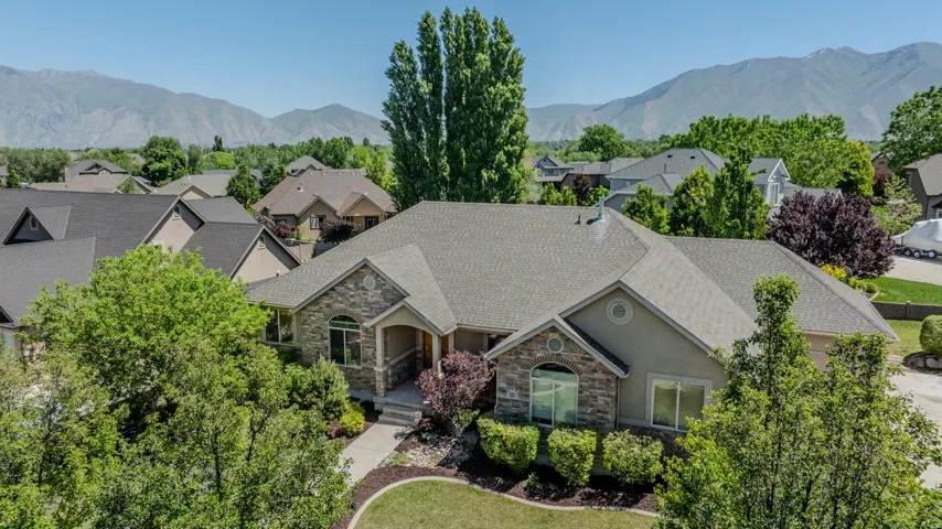 Single-story residence featuring a stone and stucco facade, a covered entry porch, a multi-gabled roofline, mature landscaping, and a mountain backdrop