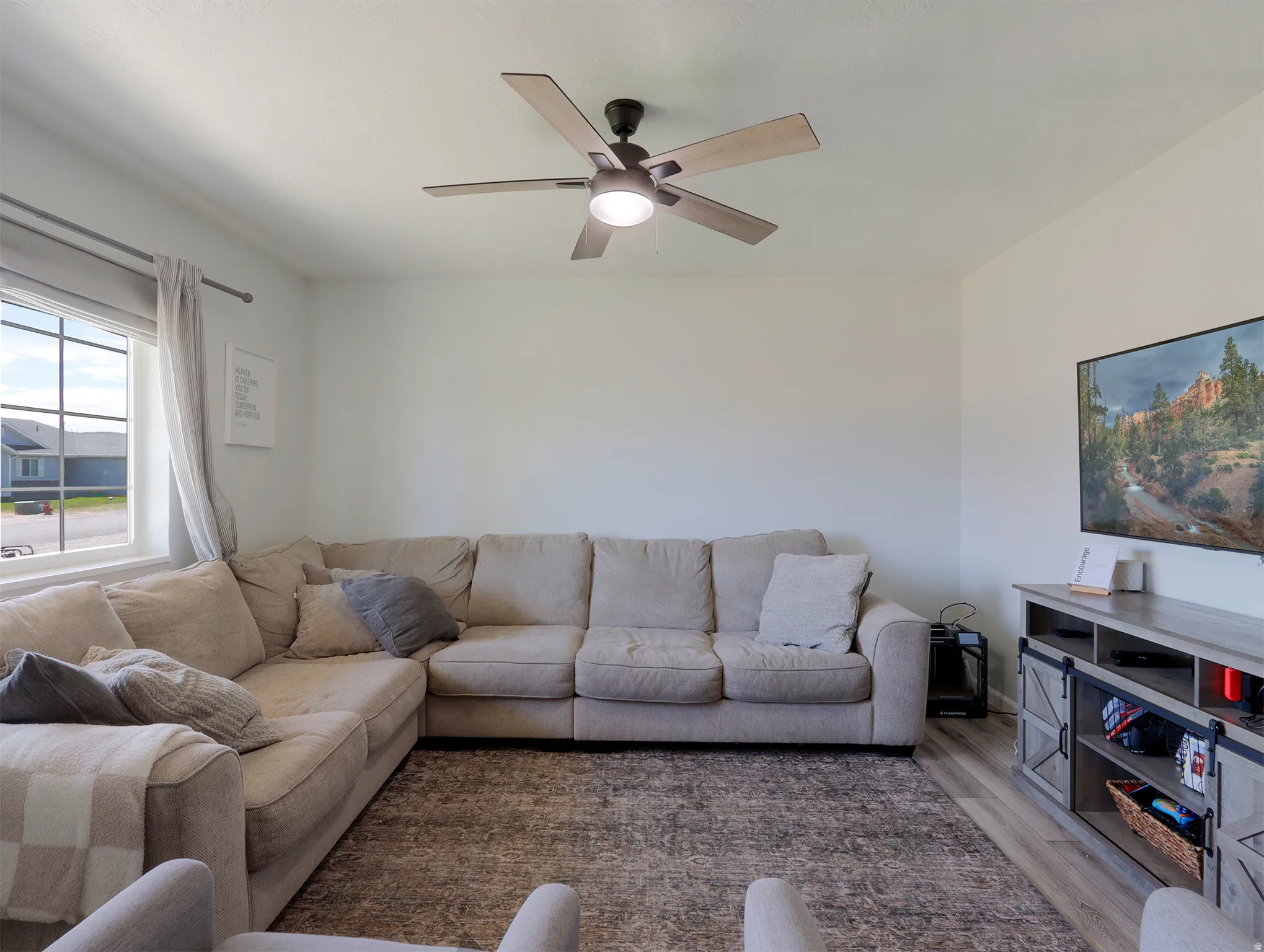 Light-filled living area featuring a ceiling fan, a large window, and wood-finish flooring
