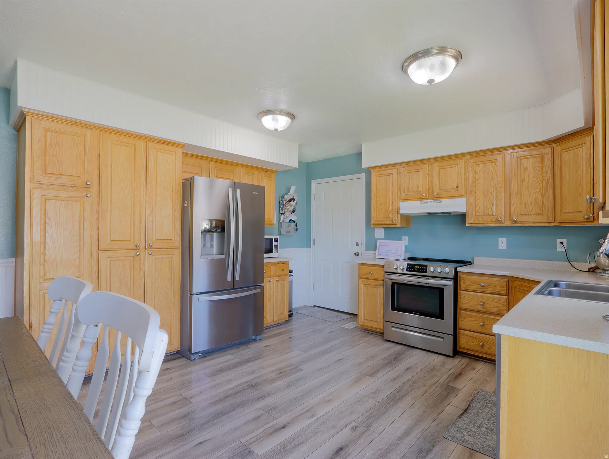 Kitchen featuring light wood cabinetry, stainless steel appliances, wood-finish flooring, light-toned countertops, and a double basin sink