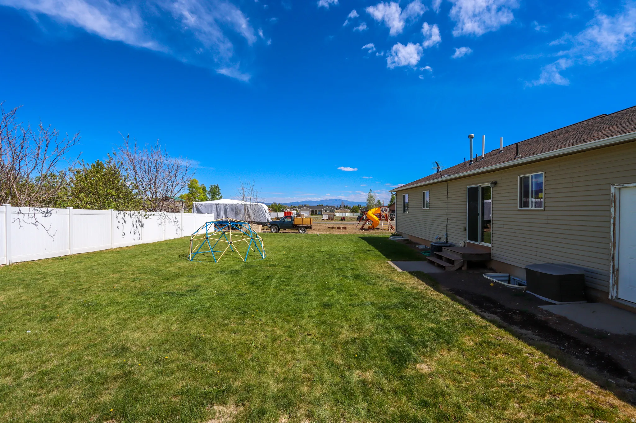 Spacious backyard featuring a manicured lawn, white privacy fencing, and a neutral-toned residential exterior