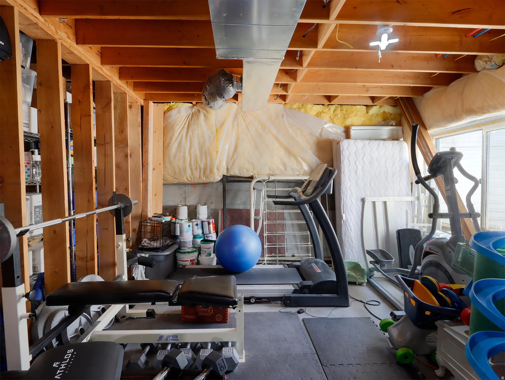 Unfinished basement space featuring exposed wood joists and structural beams, concrete foundation walls, and visible ductwork