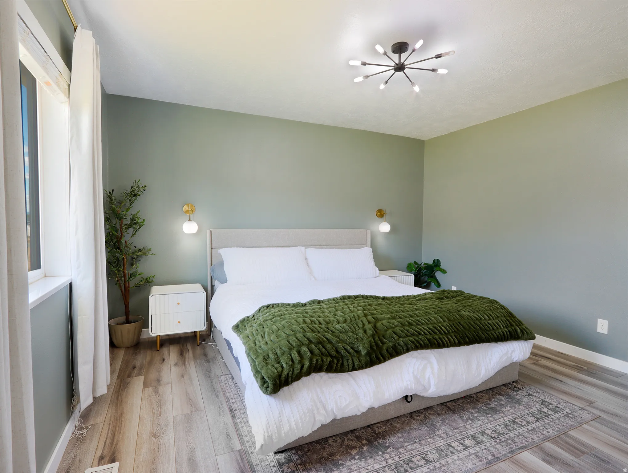 Spacious room featuring wood-finish flooring, a contemporary ceiling light fixture, and large windows with white curtains
