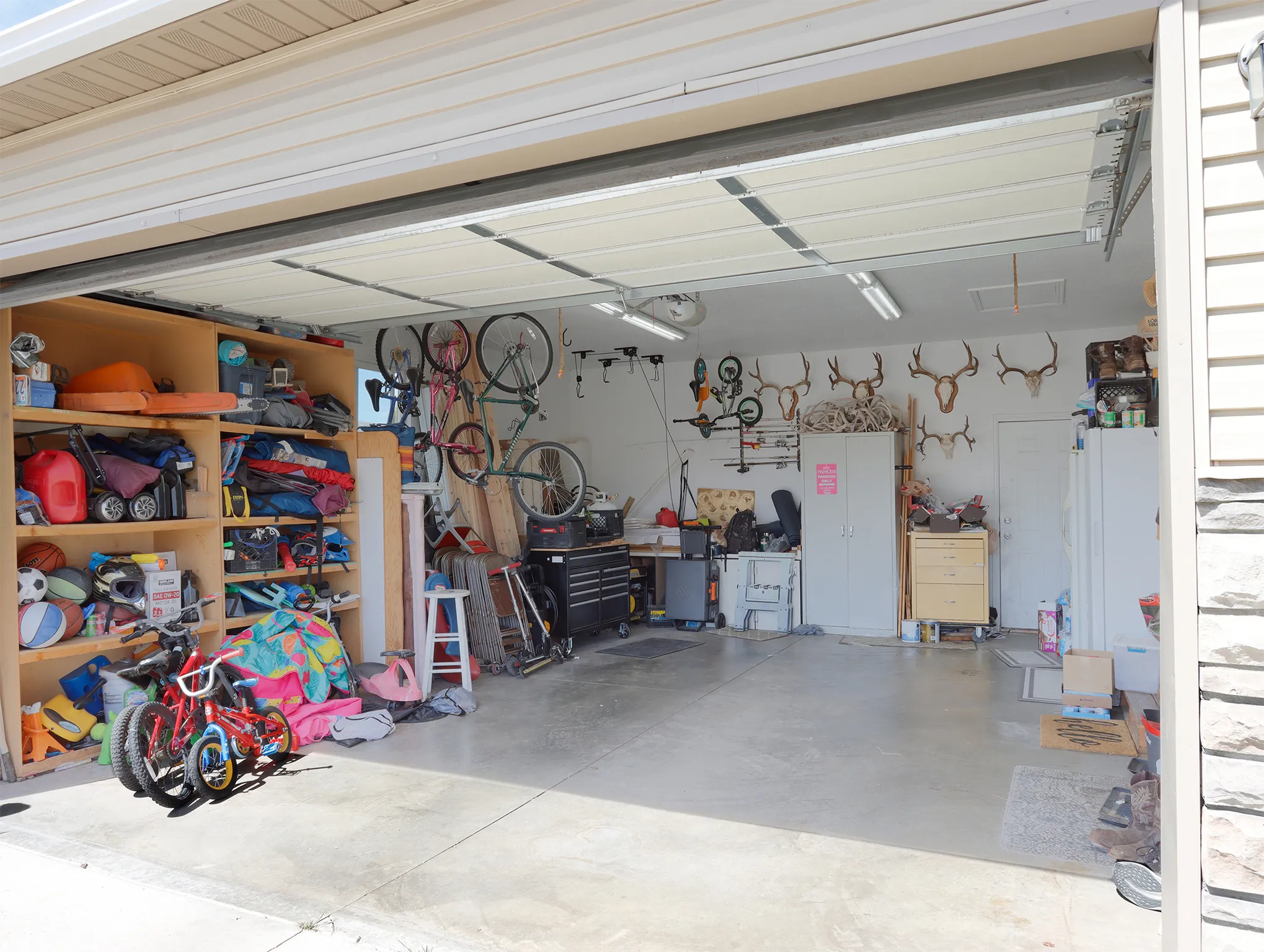 Attached two-car garage with a concrete floor, built-in wooden shelving, fluorescent lighting, and a paneled overhead door